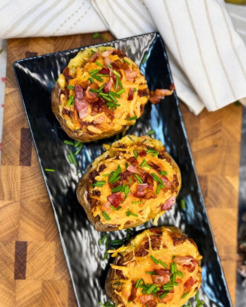 Loaded baked potatoes with crispy bacon, melted cheddar cheese, and fresh chives served on a black platter
