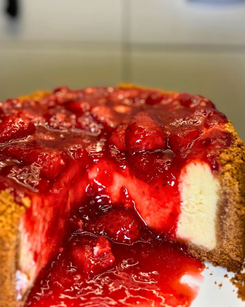 Classic baked strawberry cheesecake with biscuit crust walls and glossy homemade strawberry topping