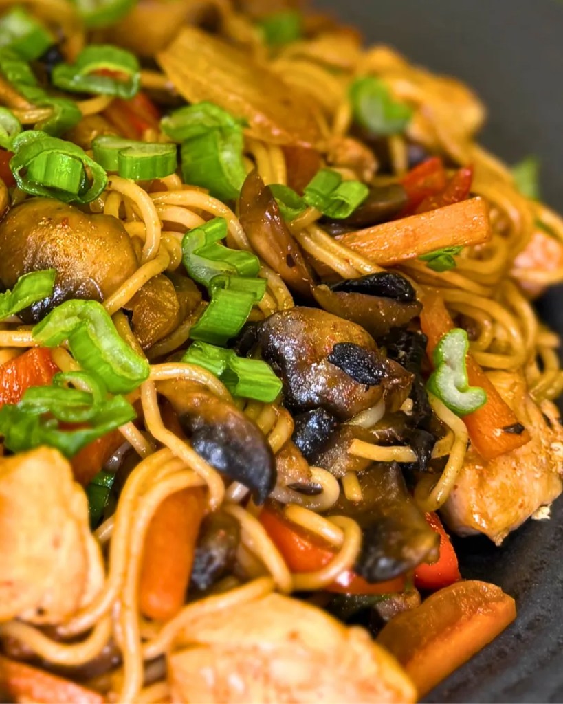 Rice noodles tossed in soy sauce with chicken, mushrooms, carrots, and fresh green onion garnish.