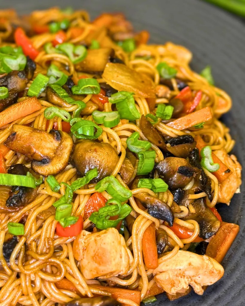 Simple chicken stir fry with rice noodles served on a gray plate, topped with fresh green onions.