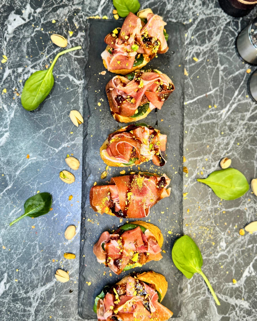 Overhead view of easy jamon serrano bruschetta topped with pistachios and balsamic glaze