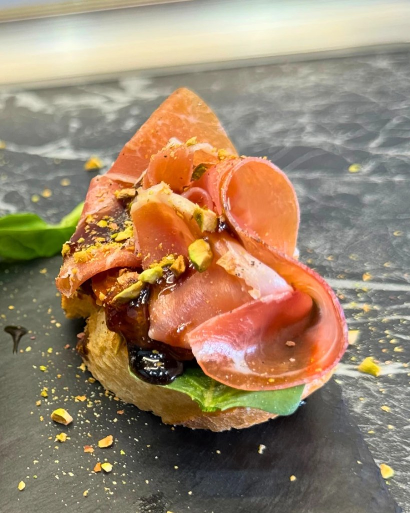 Close-up of easy jamon serrano bruschetta with spinach, sun-dried tomatoes, pistachios and balsamic glaze