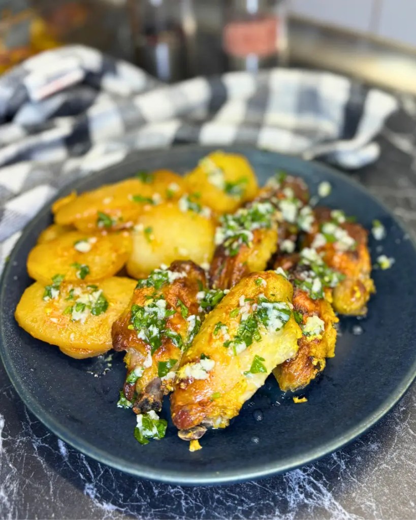 Plate of easy oven baked lemon garlic chicken wings topped with fresh parsley sauce and served with roasted potatoes
