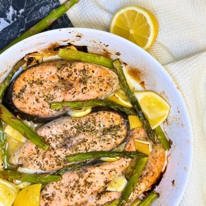 Juicy baked trout steaks topped with herbs and surrounded by roasted asparagus and lemon