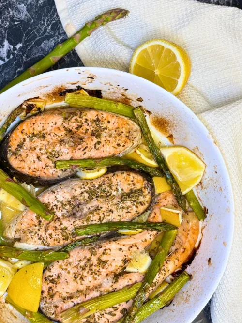 Juicy baked trout steaks topped with herbs and surrounded by roasted asparagus and lemon