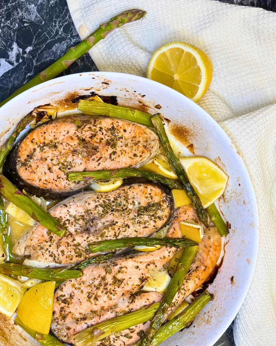 Juicy baked trout steaks topped with herbs and surrounded by roasted asparagus and lemon