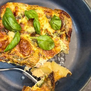 Homemade chicken quiche slice served on a dark plate, topped with fresh basil and showing a soft potato base.