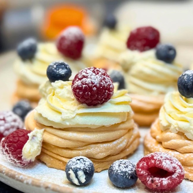 Close-up of individual mini pavlovas with crisp meringue shells, creamy mascarpone topping, and fresh berries.