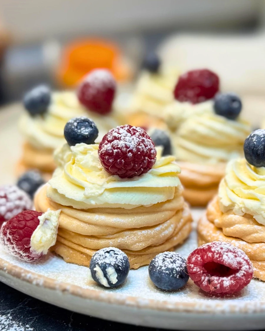 Close-up of individual mini pavlovas with crisp meringue shells, creamy mascarpone topping, and fresh berries.
