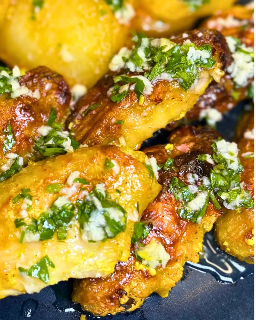 Golden oven baked lemon garlic chicken wings topped with fresh parsley and served with crispy potatoes