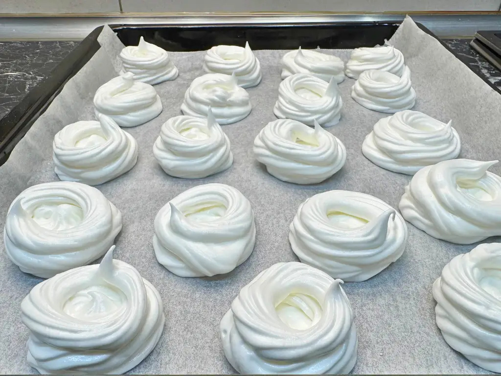 Piped mini pavlova meringue nests arranged on a baking tray lined with parchment paper