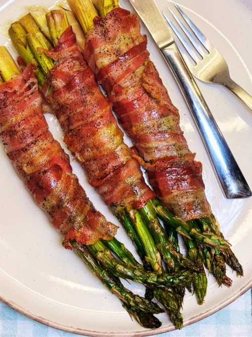 Oven baked bacon wrapped asparagus bundles with crispy bacon and tender roasted asparagus, served on a plate as an easy side dish.