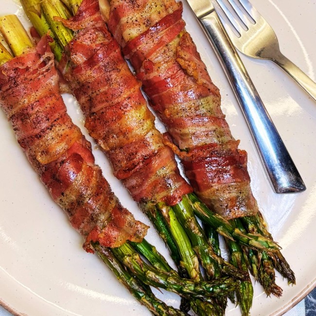 Oven baked bacon wrapped asparagus bundles with crispy bacon and tender roasted asparagus, served on a plate as an easy side dish.