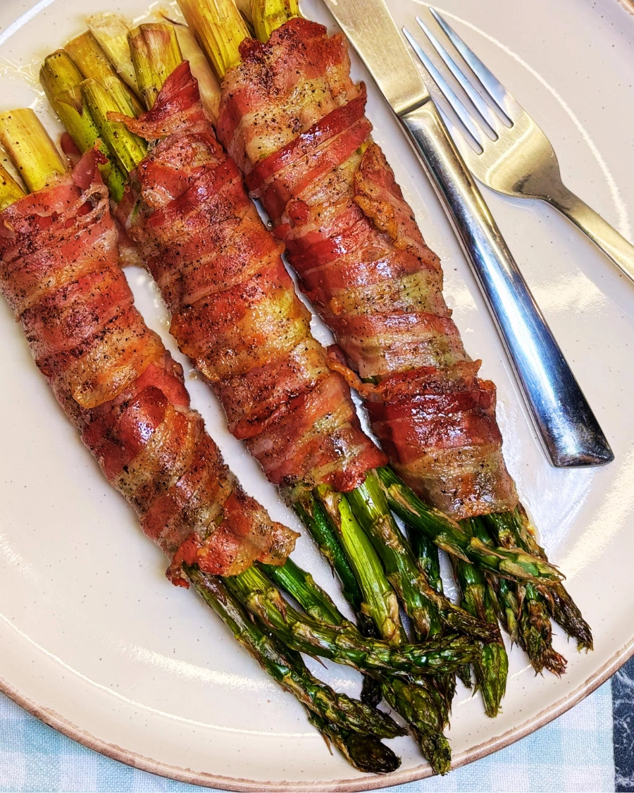 Oven baked bacon wrapped asparagus bundles with crispy bacon and tender roasted asparagus, served on a plate as an easy side dish.