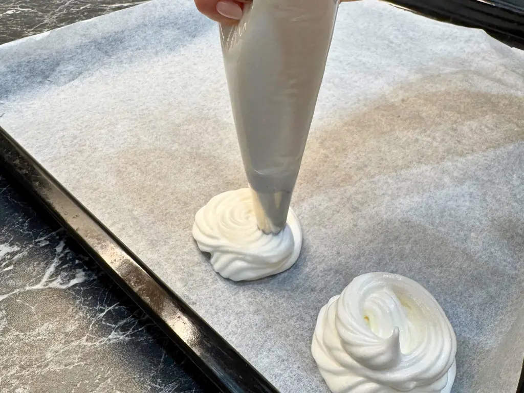 Piping mini pavlova nests onto a baking tray using a piping bag