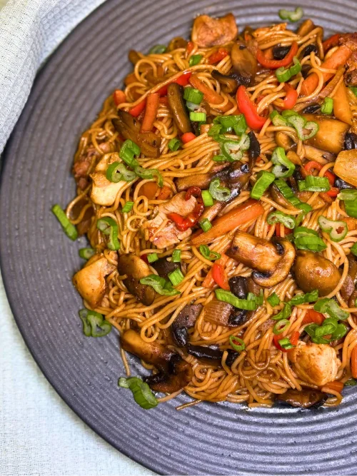 Simple chicken stir fry with rice noodles served on a gray plate, topped with fresh green onions.