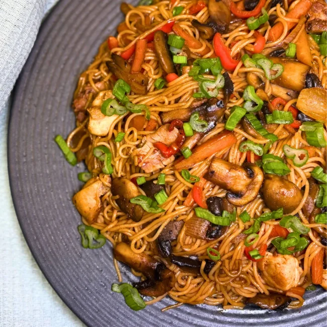 Simple chicken stir fry with rice noodles served on a gray plate, topped with fresh green onions.