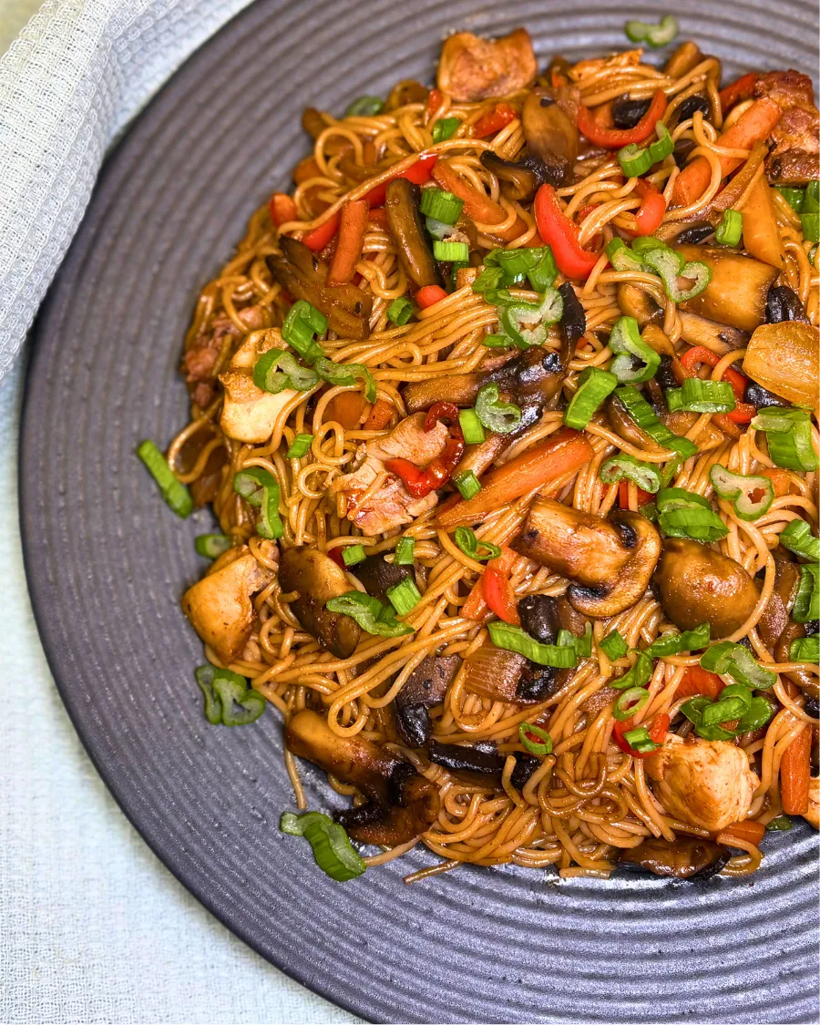 Simple chicken stir fry with rice noodles served on a gray plate, topped with fresh green onions.