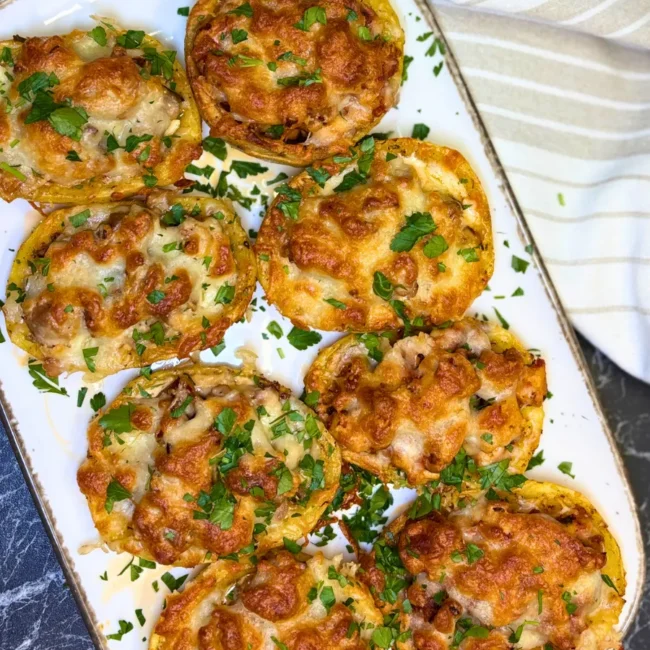 Top view of baked stuffed potatoes with chicken, topped with melted golden cheese and fresh parsley on a white serving plate.