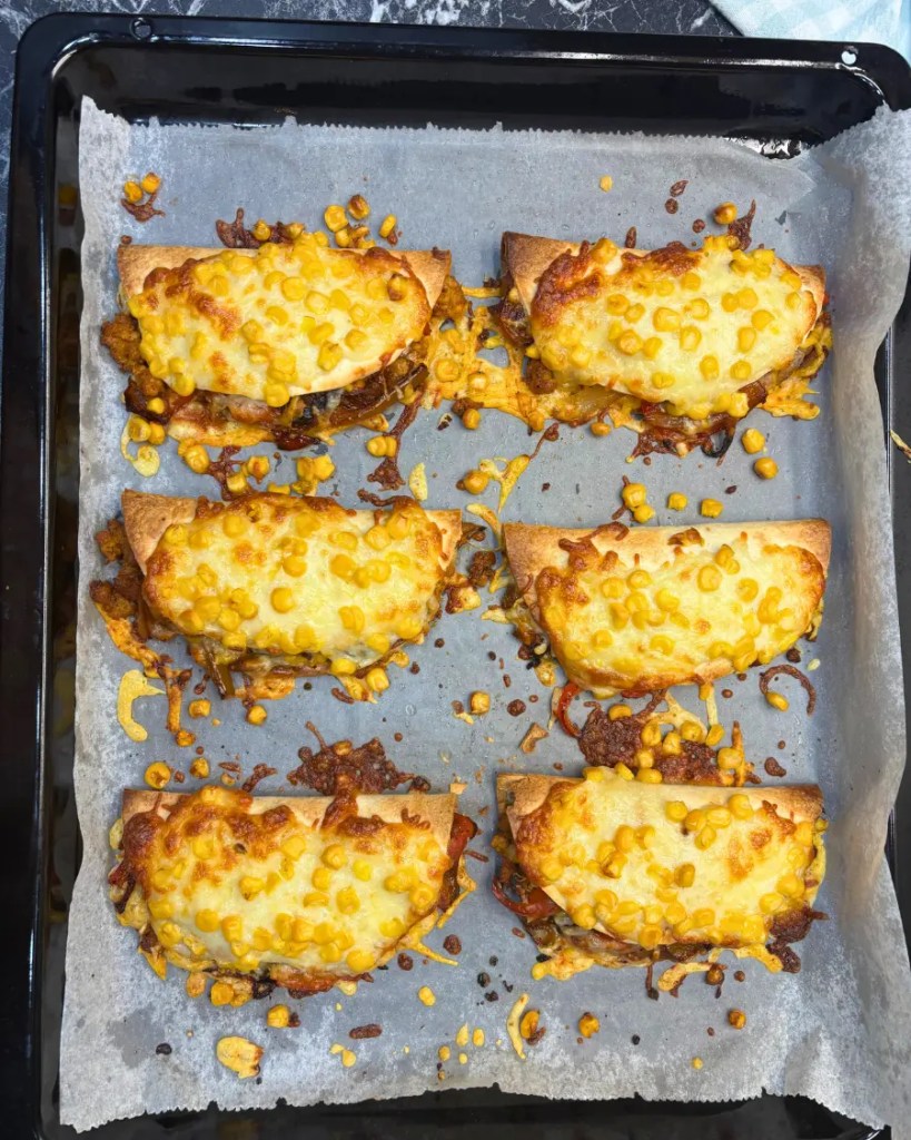 crispy baked chicken tacos with melted cheese and corn on a baking tray