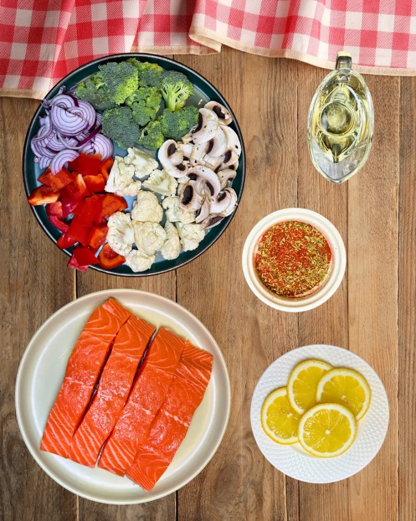 ingredients for salmon and vegetables in parchment paper including salmon broccoli mushrooms peppers and lemon