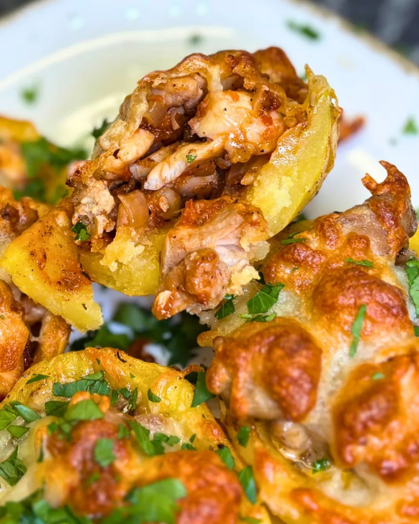 Close-up of a stuffed potato cut open, showing juicy chicken filling, onions, creamy sauce, and melted cheese inside a soft baked potato shell.