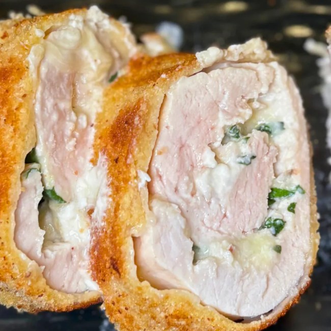 Juicy turkey roulade slices with creamy cheese and spinach filling on a black plate