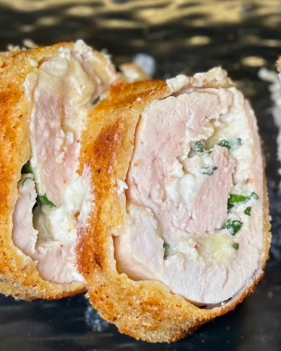 Juicy turkey roulade slices with creamy cheese and spinach filling on a black plate