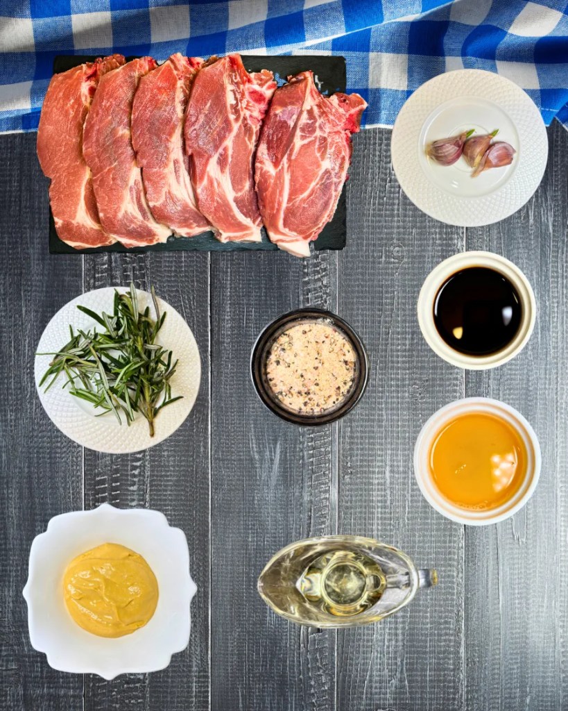 Raw pork steaks with mustard, honey, soy sauce, garlic, rosemary, and seasonings arranged on a table for air fryer recipe