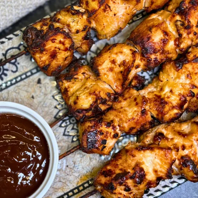 Close-up of juicy smoky air fryer chicken skewers garnished with fresh red onion slices