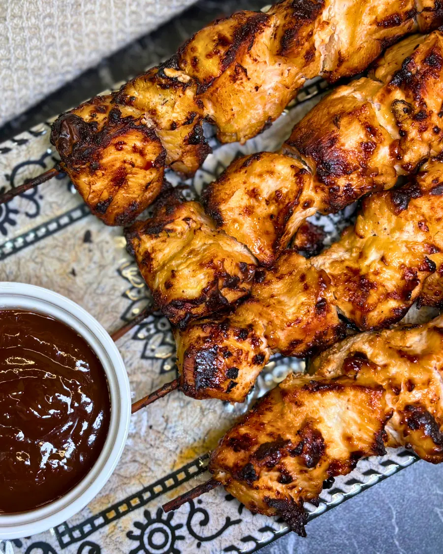 Close-up of juicy smoky air fryer chicken skewers garnished with fresh red onion slices