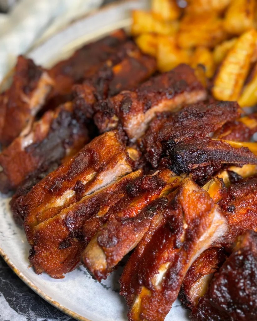 Close-up of juicy sticky honey soy pork ribs with caramelized glaze served with crispy potatoes.