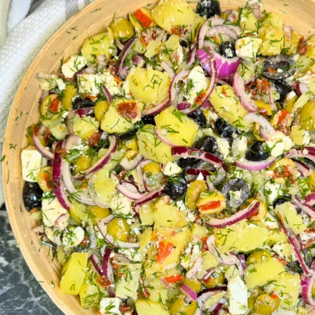 Homemade potato feta salad served in a wooden bowl with olives, dill, and sun dried tomatoes.