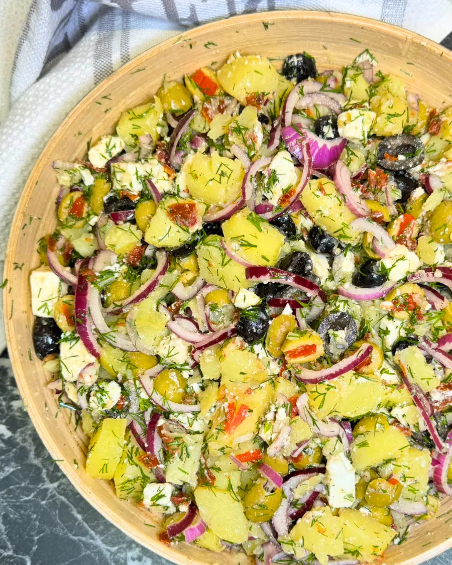 Homemade potato feta salad served in a wooden bowl with olives, dill, and sun dried tomatoes.