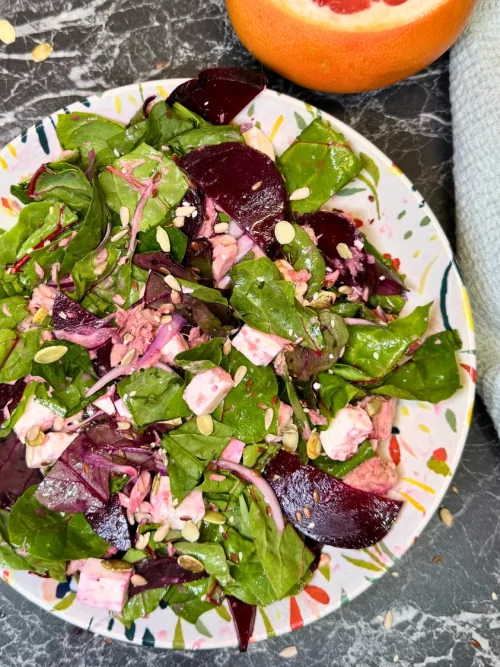 Top view of beetroot and tuna salad with leafy greens, feta cubes, pumpkin seeds and fresh grapefruit on the side