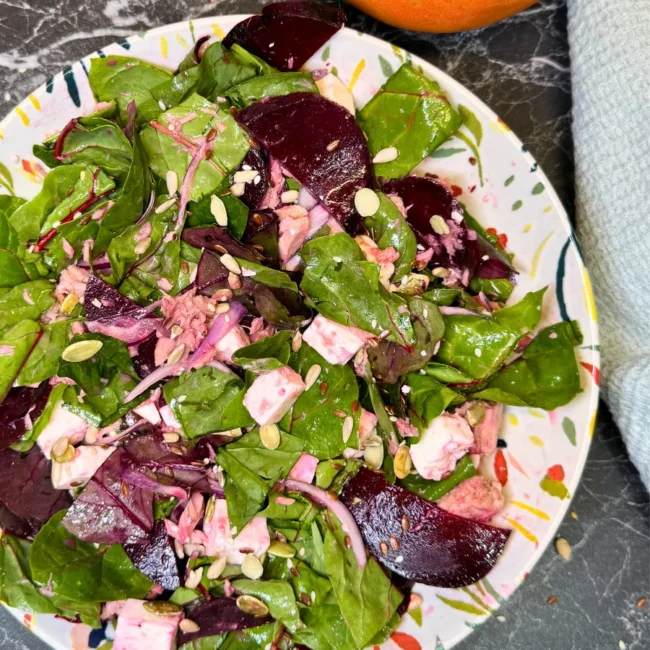 Top view of beetroot and tuna salad with leafy greens, feta cubes, pumpkin seeds and fresh grapefruit on the side