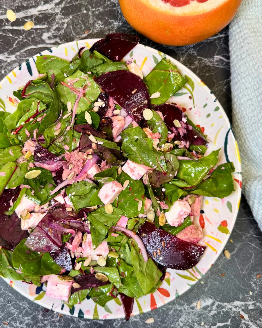 Top view of beetroot and tuna salad with leafy greens, feta cubes, pumpkin seeds and fresh grapefruit on the side