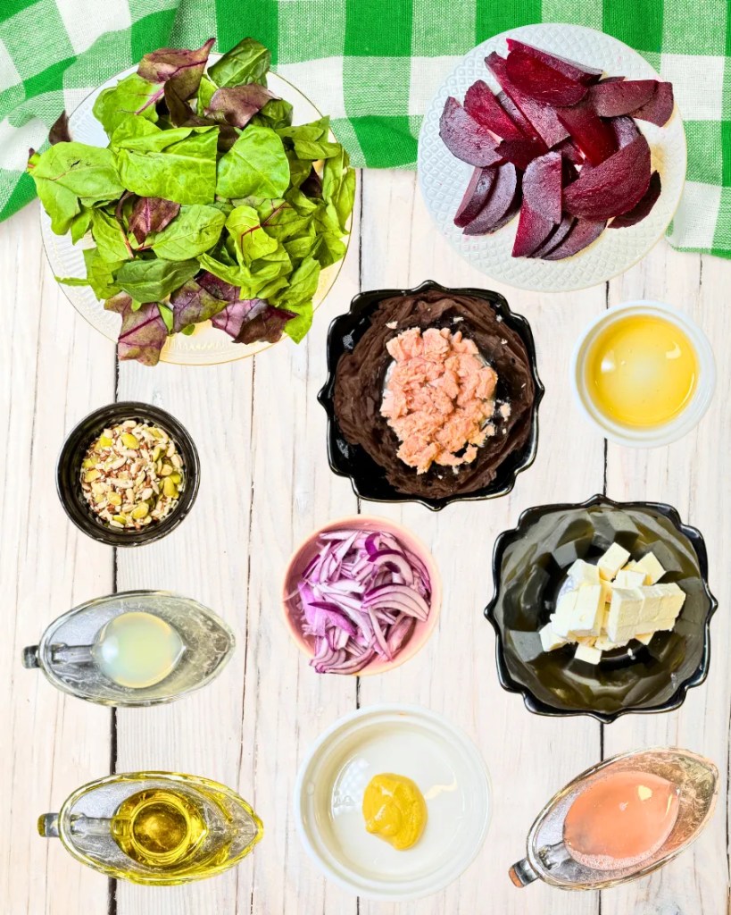 Fresh ingredients for beetroot tuna salad including greens, beetroot, tuna, feta, red onion, seeds, and citrus dressing components