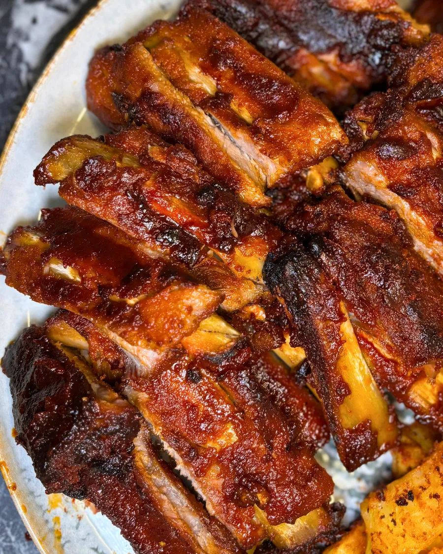 Close-up of tender sticky pork ribs coated in a rich honey soy glaze with crispy roasted potatoes.