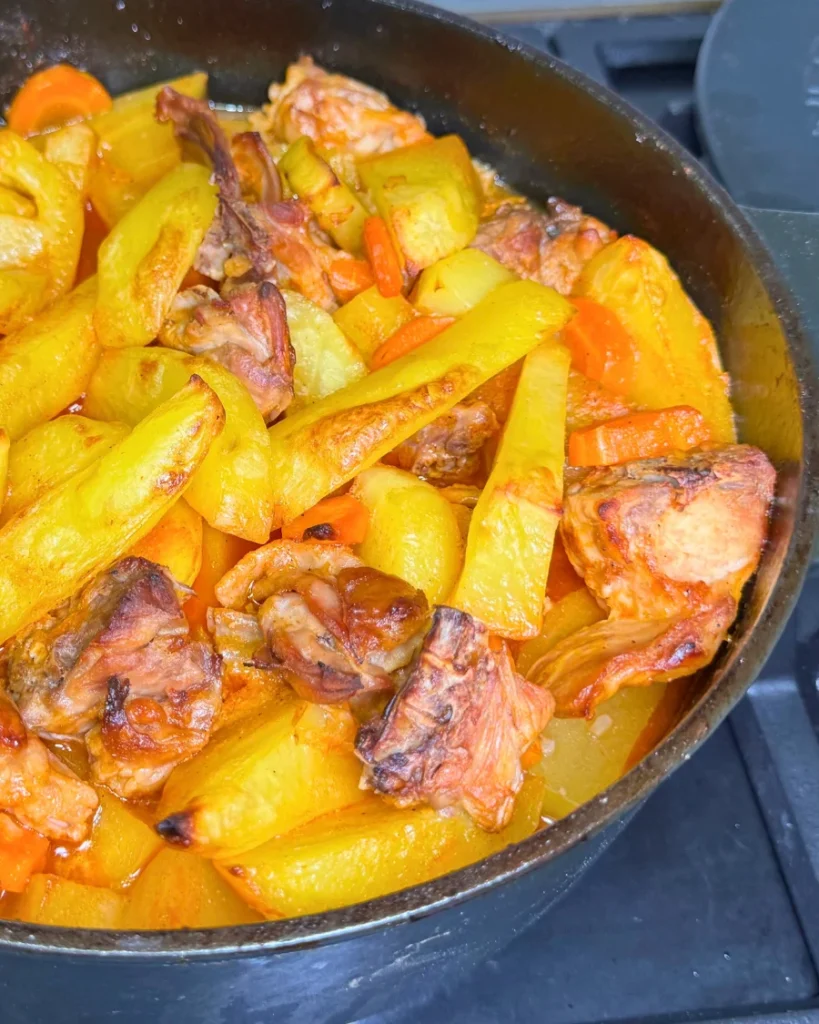 Angled view of a cast-iron pot filled with braised rabbit, golden potatoes, carrots, and tomato sauce.