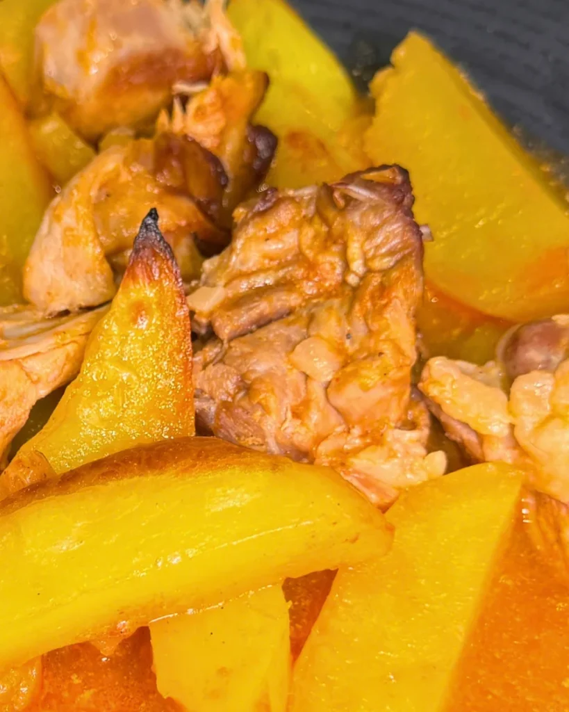 Close-up of tender rabbit pieces and golden potato wedges coated in tomato sauce.