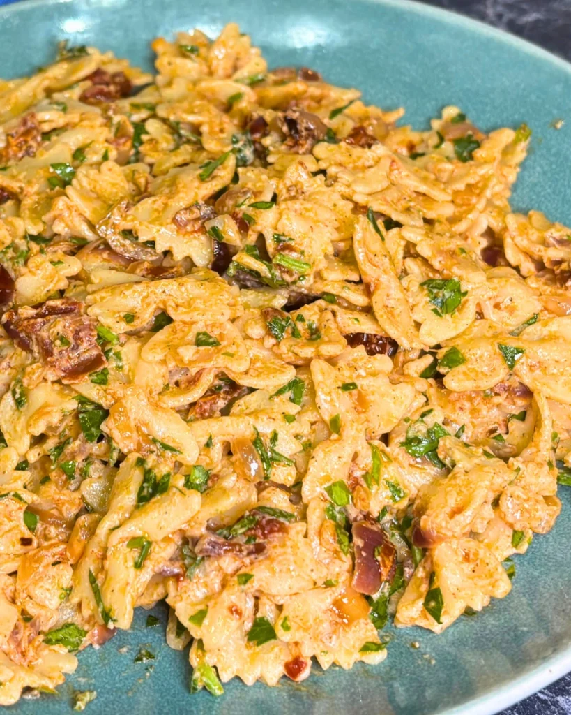 Close-up of creamy onion pasta with caramelized onions, sun-dried tomatoes, and chopped parsley