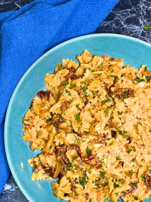 Close-up of creamy farfalle pasta coated in roasted onion sauce with sun-dried tomatoes and parsley
