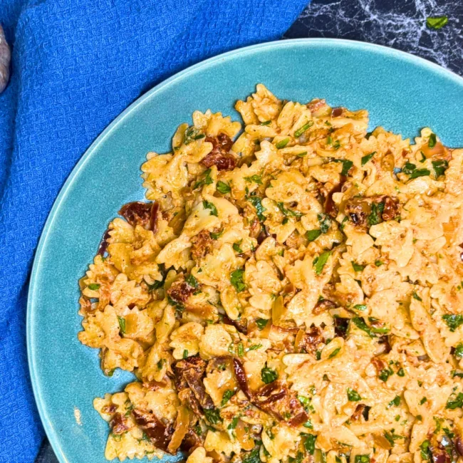 Close-up of creamy farfalle pasta coated in roasted onion sauce with sun-dried tomatoes and parsley