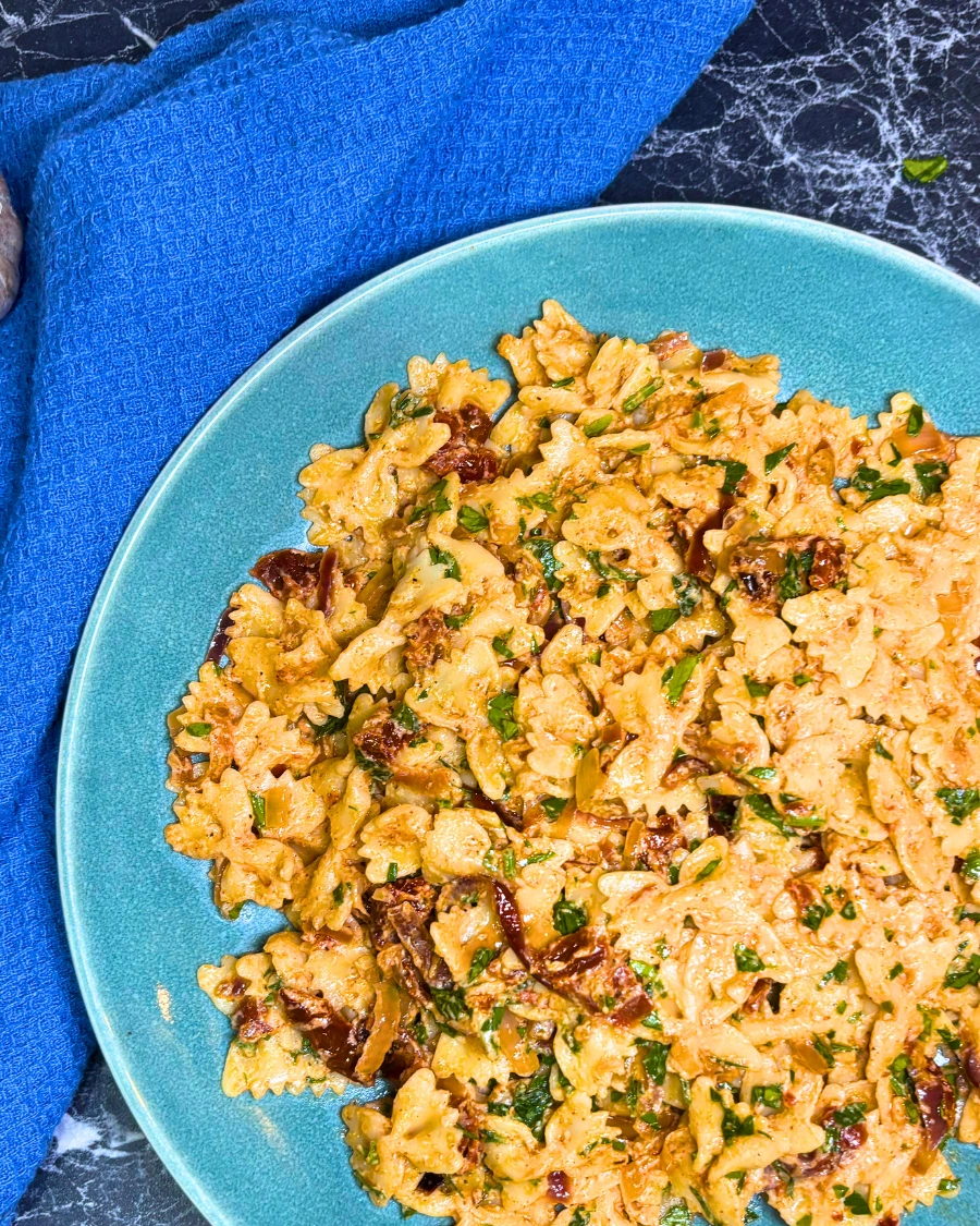 Close-up of creamy farfalle pasta coated in roasted onion sauce with sun-dried tomatoes and parsley