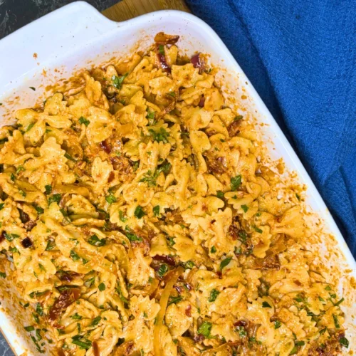 Creamy farfalle pasta with roasted onions, sun-dried tomatoes, cream cheese, and chopped parsley