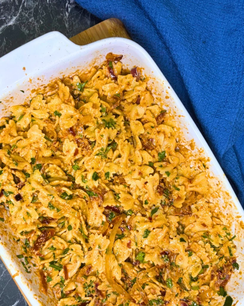 Creamy farfalle pasta with roasted onions, sun-dried tomatoes, cream cheese, and chopped parsley
