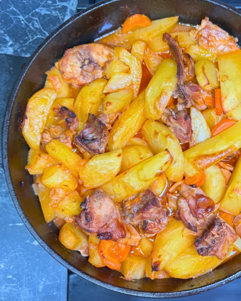 Overhead view of oven-braised rabbit with golden potatoes and carrots in a cast-iron pot.