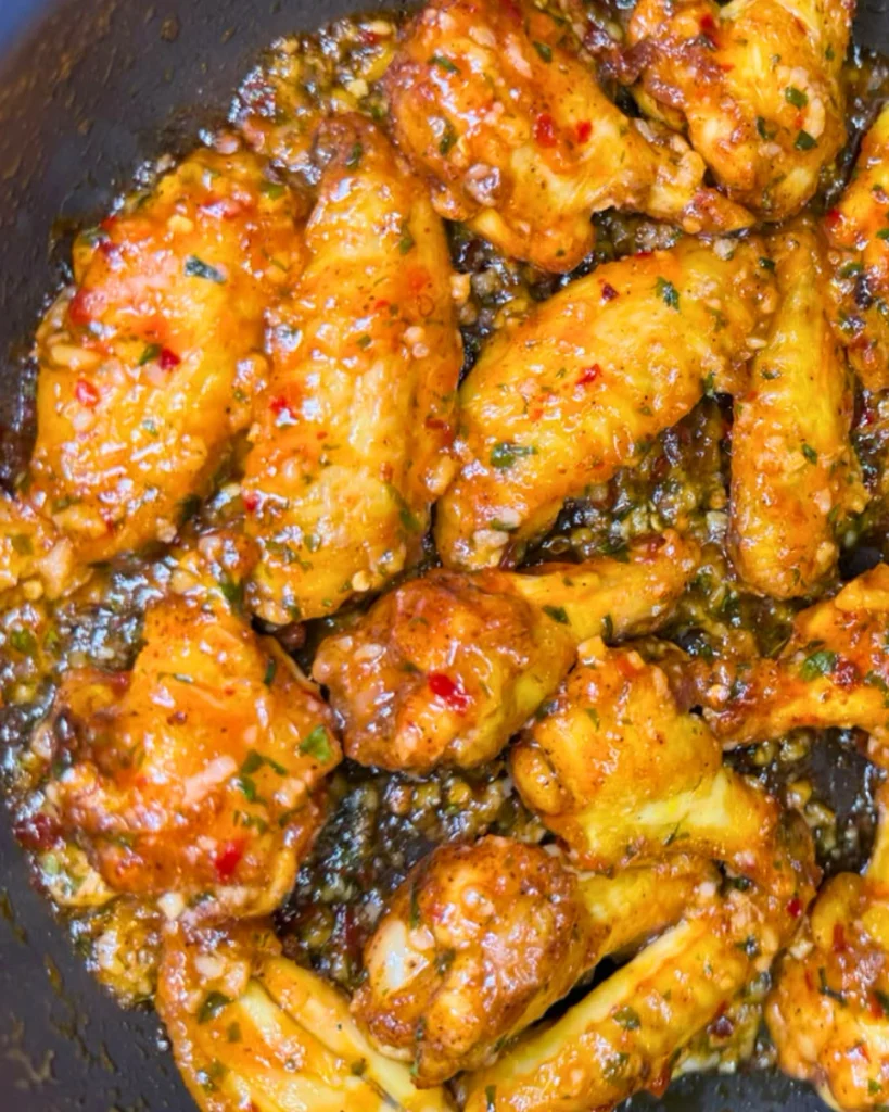 Close-up of crispy chicken wings covered in a glossy sweet chili garlic sauce with chili flakes.