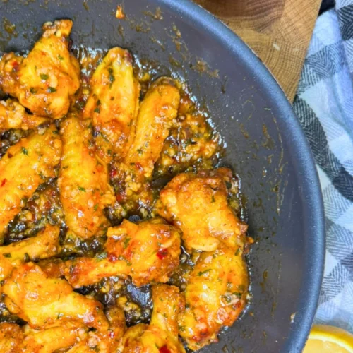 Sticky air fryer sweet chili chicken wings served on a plate with a fresh lemon wedge.